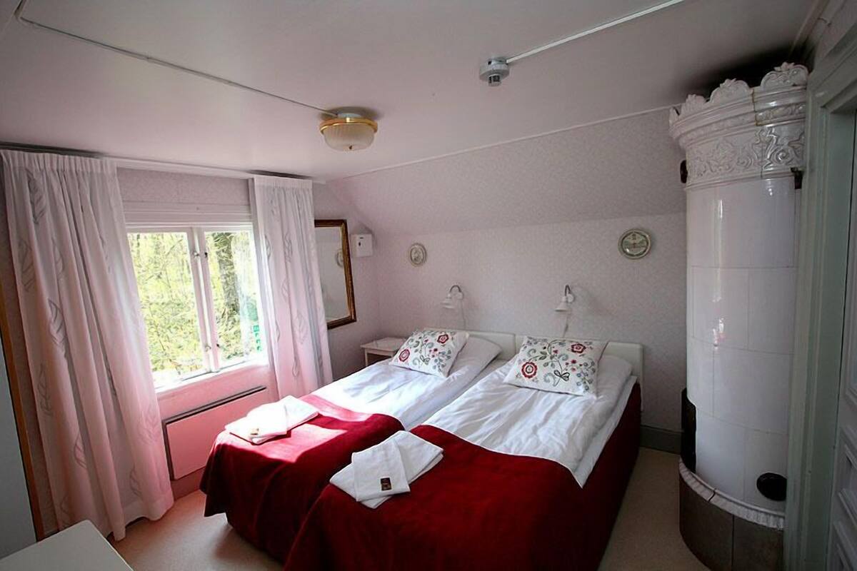 A room with two beds, a window with curtains, a mirror, and a white column.