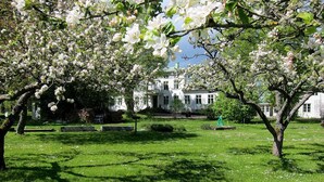 A garden with blooming trees and a white building in the background. - Drottning Victorias Hotell och Vilohem (Borgholm)