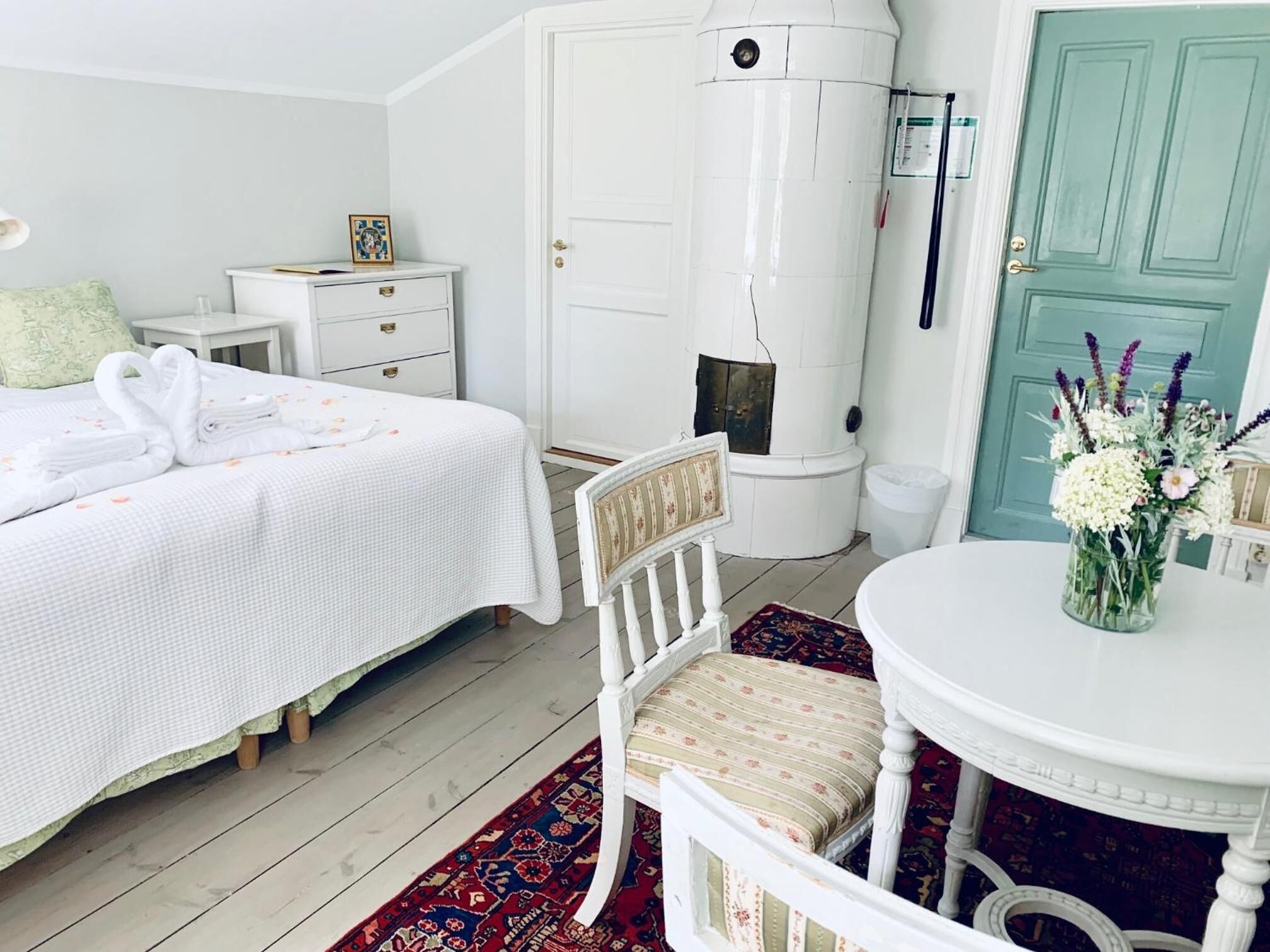 A bedroom with a bed, a chair, a table, a white cabinet, and a green door.
