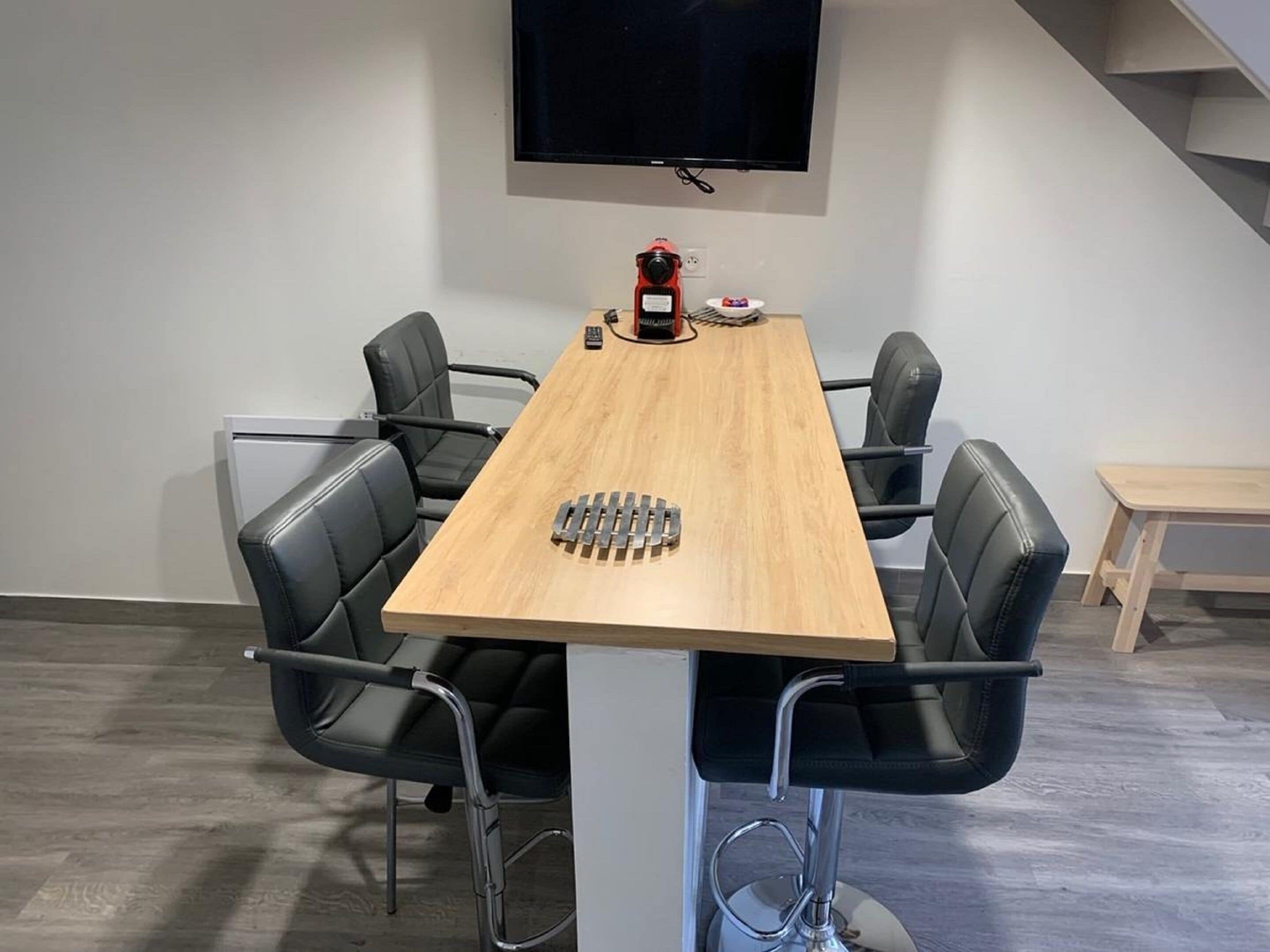 A conference room with a wooden table, black chairs, a TV mounted on the wall, and a small table with a red object on it.