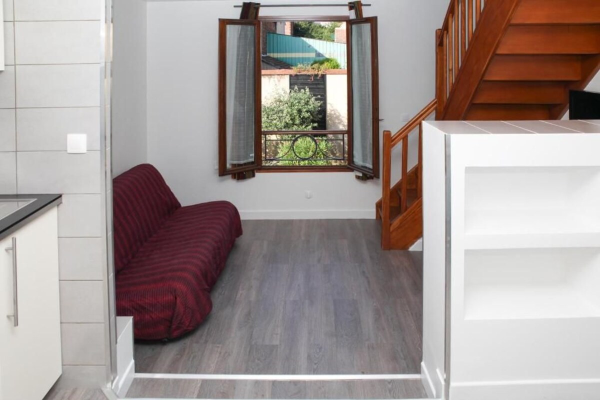 A room with a bed, a window with curtains, a staircase, and a view of the outside.