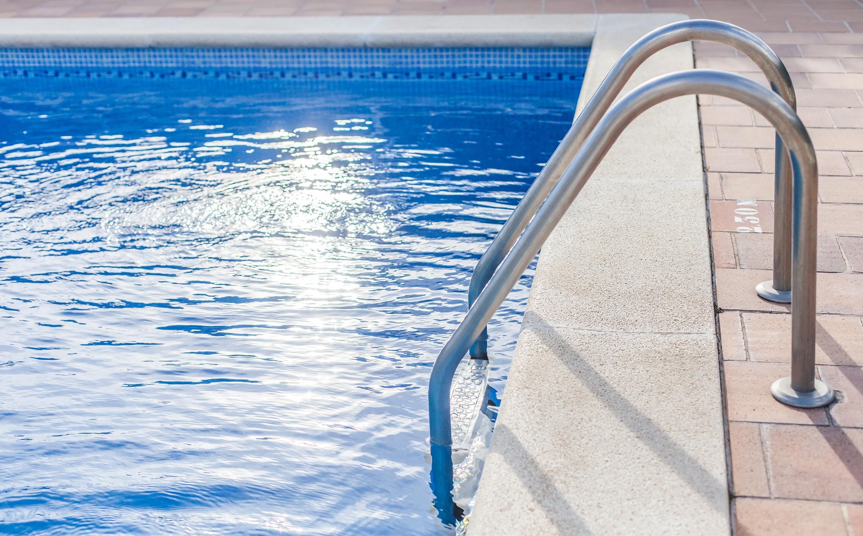 A swimming pool with metal handrails and a tiled edge.