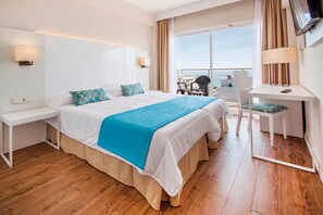 Habitación de hotel con una cama grande, un escritorio con una silla, un televisor y vistas al mar.