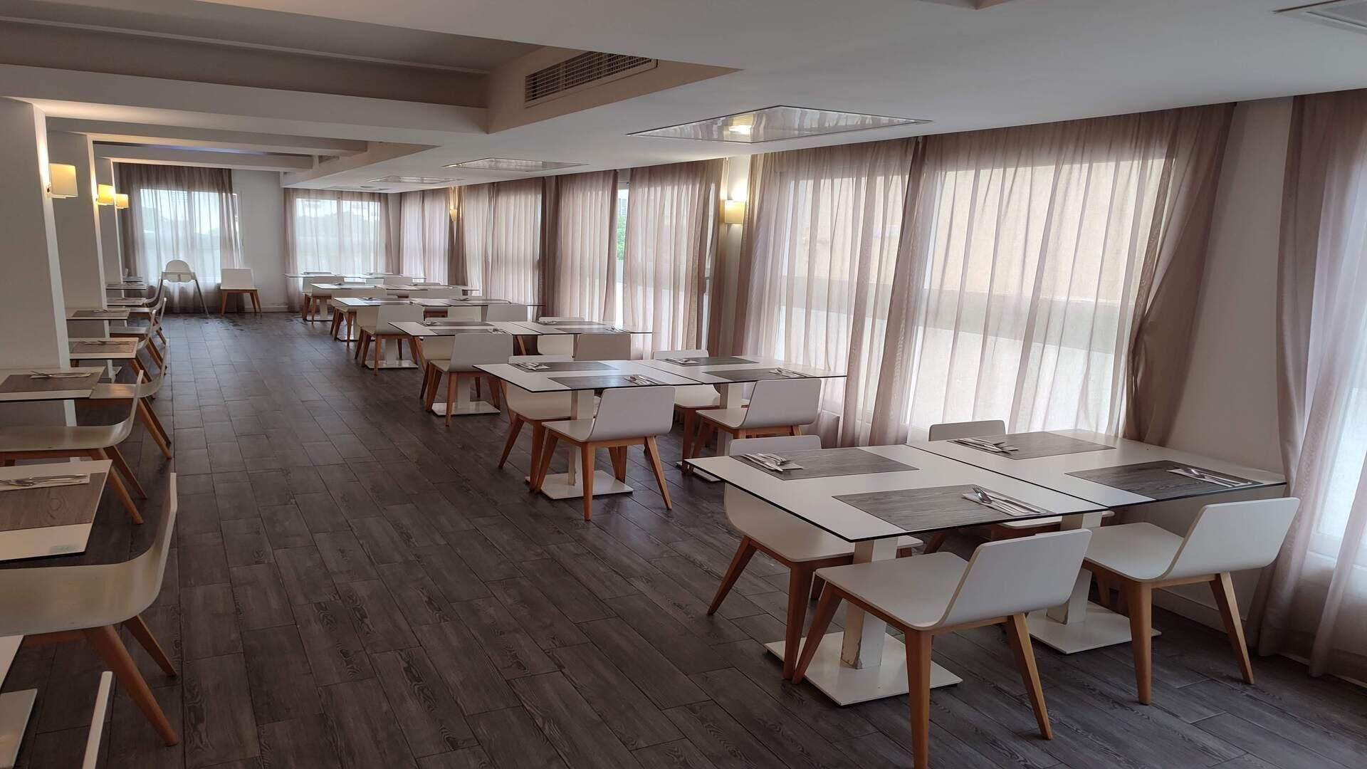 Una amplia sala de conferencias con largas mesas y sillas, ventanas grandes con cortinas translúcidas y un diseño moderno del techo.