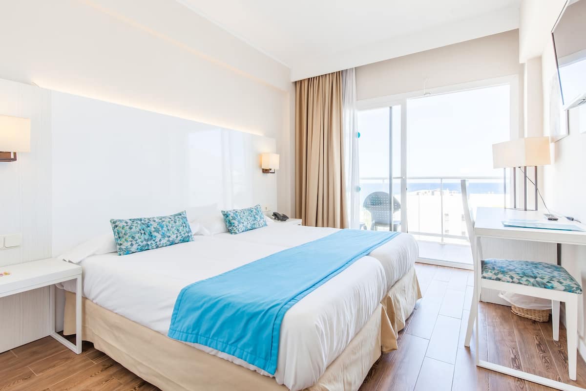 A hotel room with a large bed, a desk, a chair, and a balcony with a view.