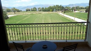 Un balcón con vista a un campo verde y montañas. Hay una mesa y dos sillas en el balcón.