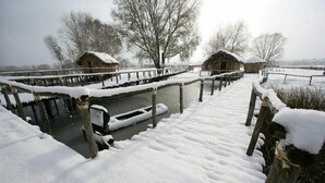 Zona exterior nevada con construcciones de madera y un canal de agua.