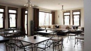 Un comedor amplio con varias mesas y sillas, un conjunto de sofás y ventanas grandes que permiten la entrada de luz natural.