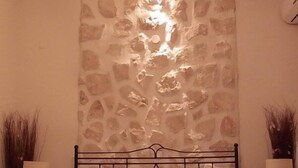 Un dormitorio con pared de piedra, una cama con ropa de cama blanca y dos mesitas de noche con lámparas.