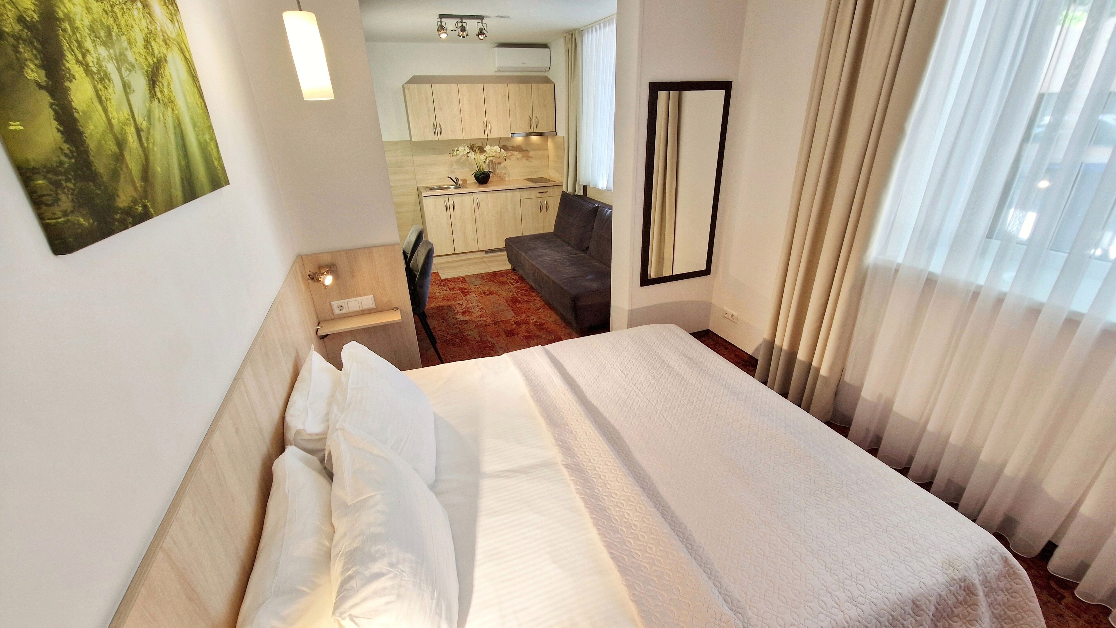 Habitación de hotel con cama, escritorio, silla, kitchenette pequeña y vistas al exterior.