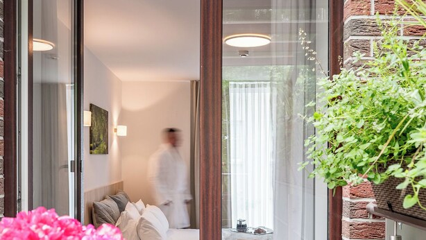 A hotel room with a bed, a window, and a view of the outside. There is a balcony with a table and chairs, and a potted plant. - HOME Apart-Hotel Vilnius (Vilnius)