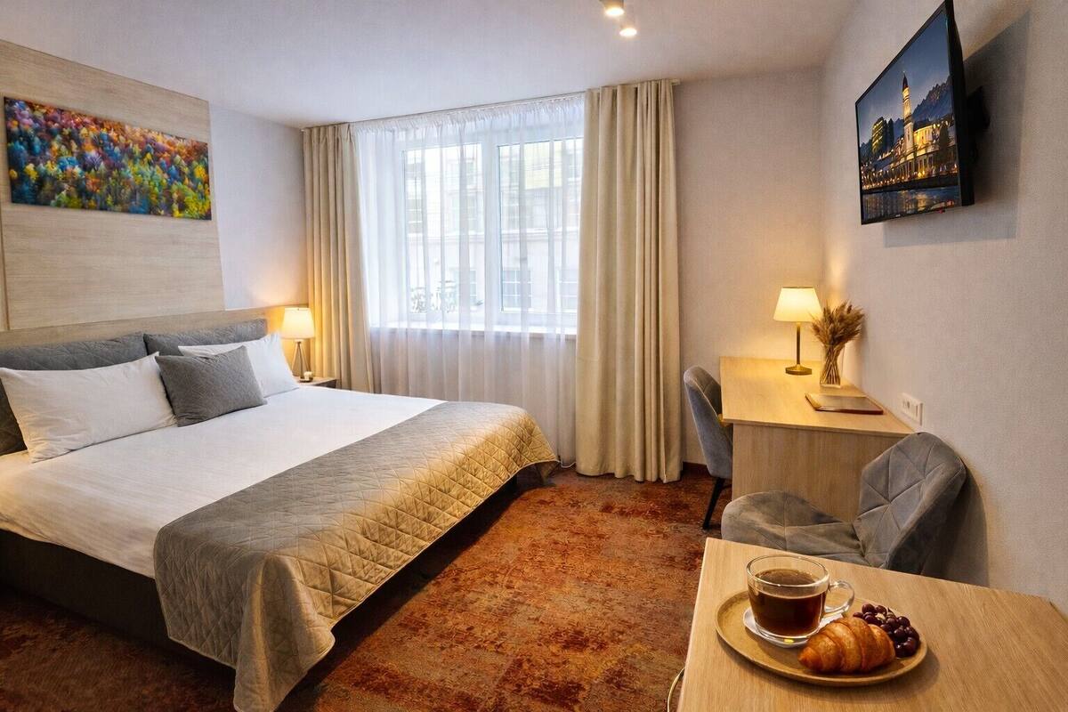 Una habitación de hotel con cama, escritorio con silla, televisor y un cuadro en la pared.
