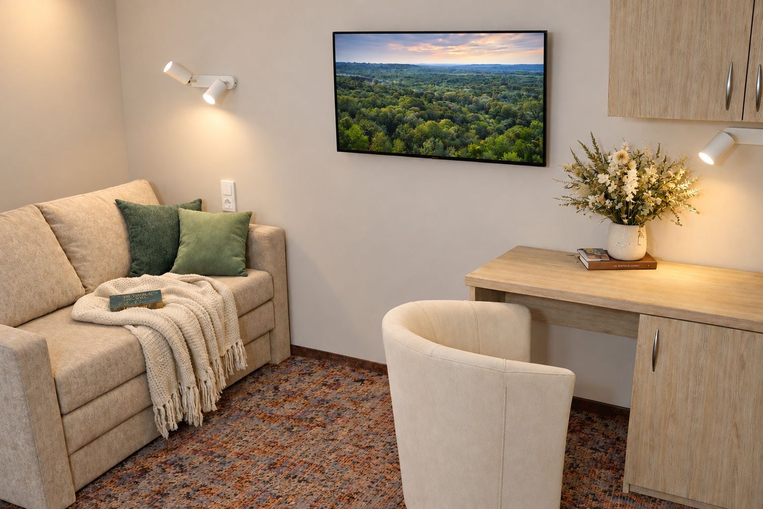 A cozy living area with a sofa, a small desk, and a chair. There is a framed landscape picture on the wall and a vase with flowers on the desk.