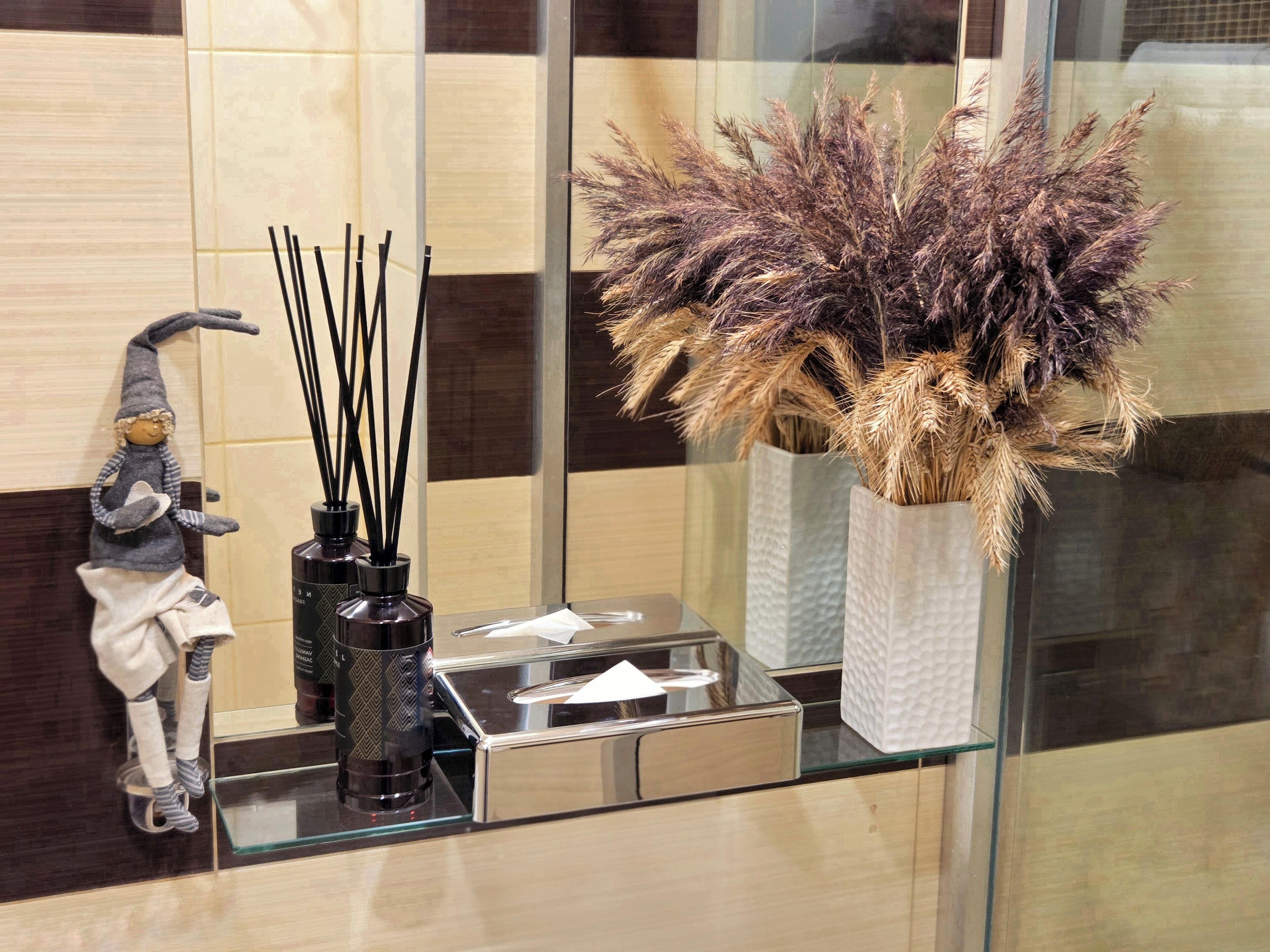 Un meuble-lavabo de salle de bain avec un miroir, une statuette de gnome décorative, un brûle-encens noir et un vase contenant des plantes séchées.