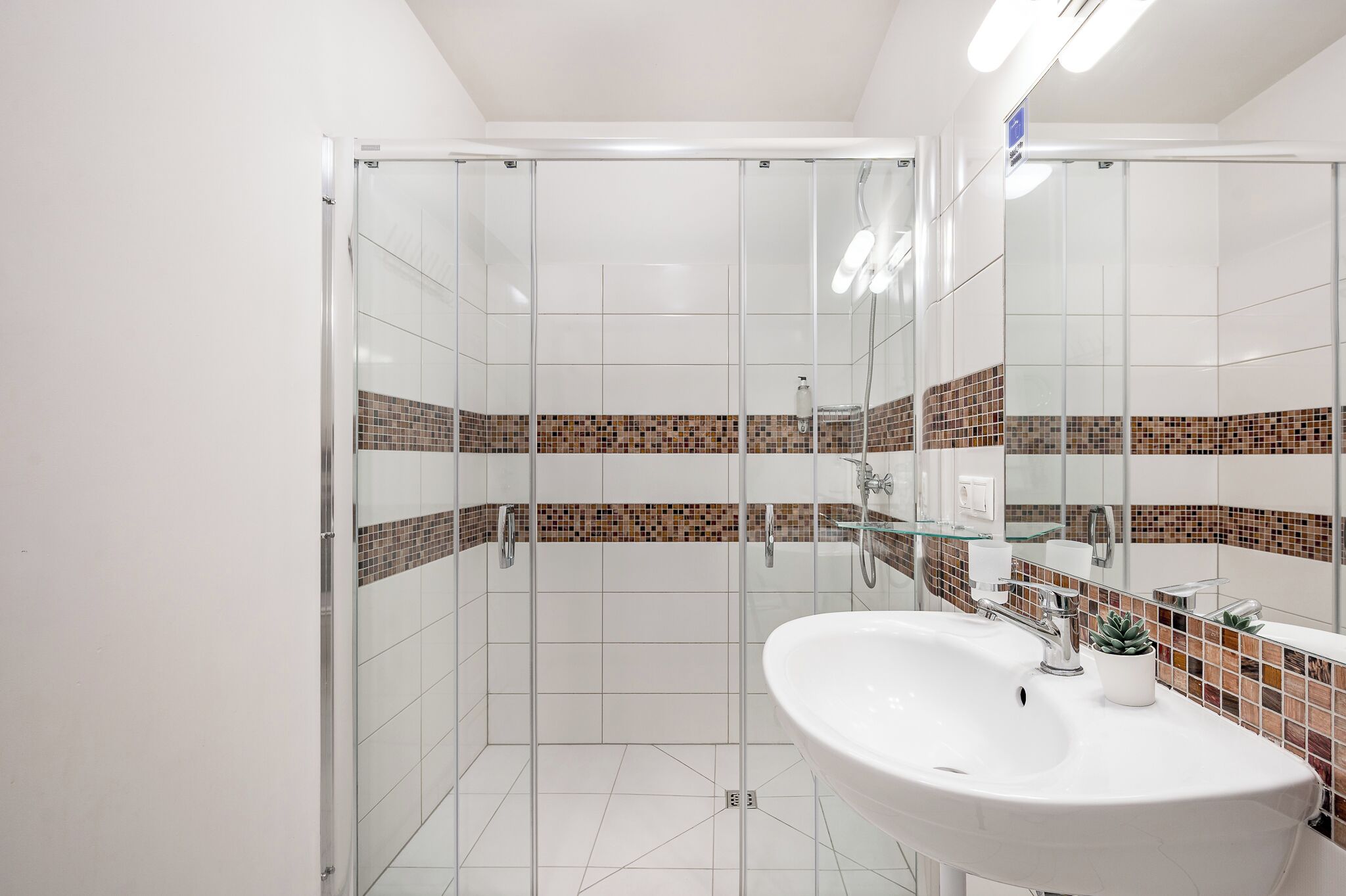 Un baño moderno con cabina de ducha de vidrio, lavamanos blanco y salpicadero de azulejos.
