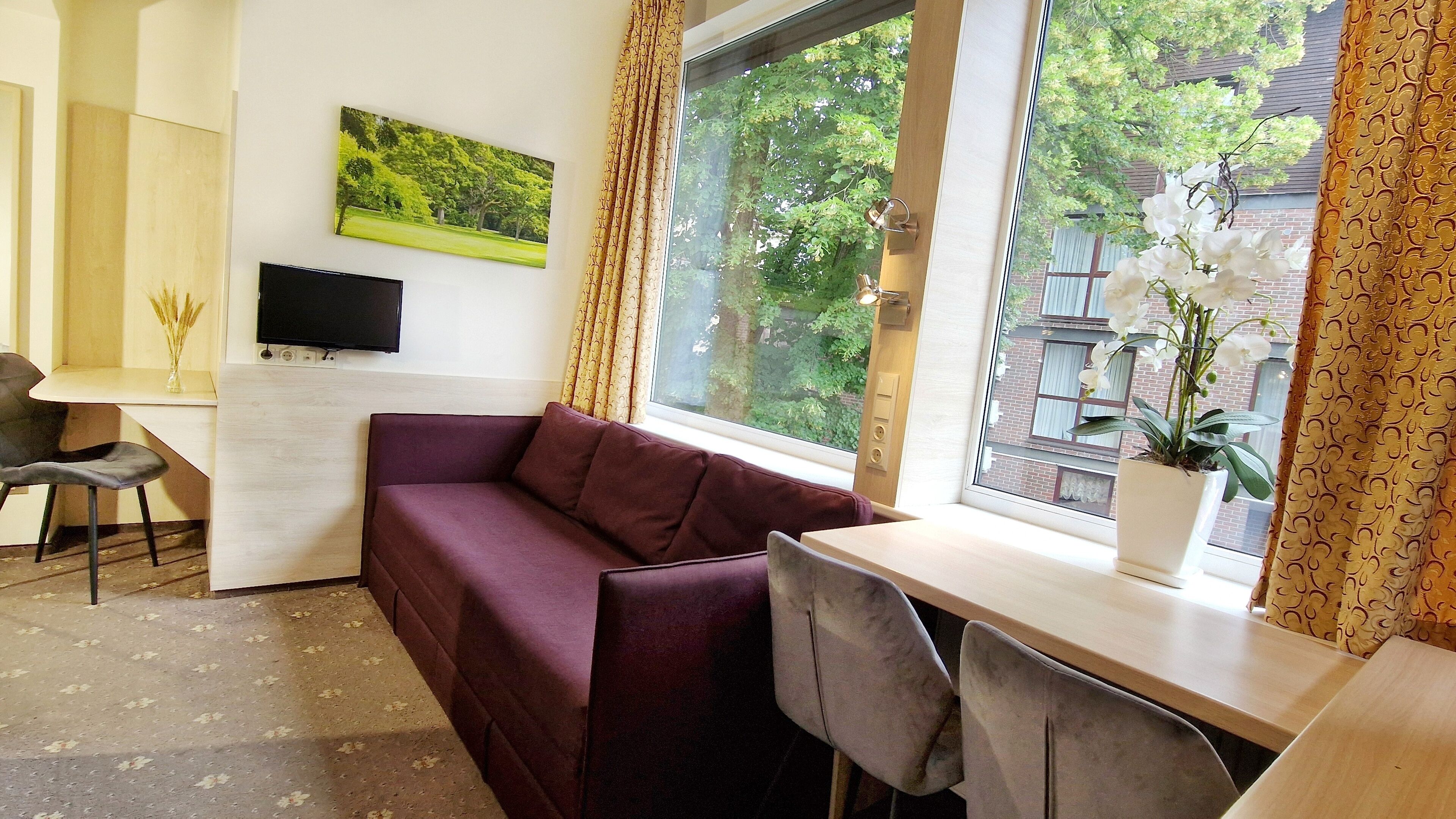 Una habitación con sofá, escritorio, silla, televisor y ventana con cortinas.