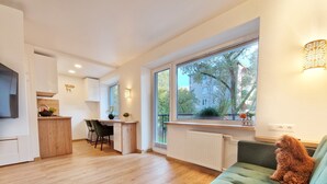 A modern apartment with a green sofa, a kitchen area, and large windows offering a view of the outside. - HOME Apart-Hotel Vilnius (Vilnius)
