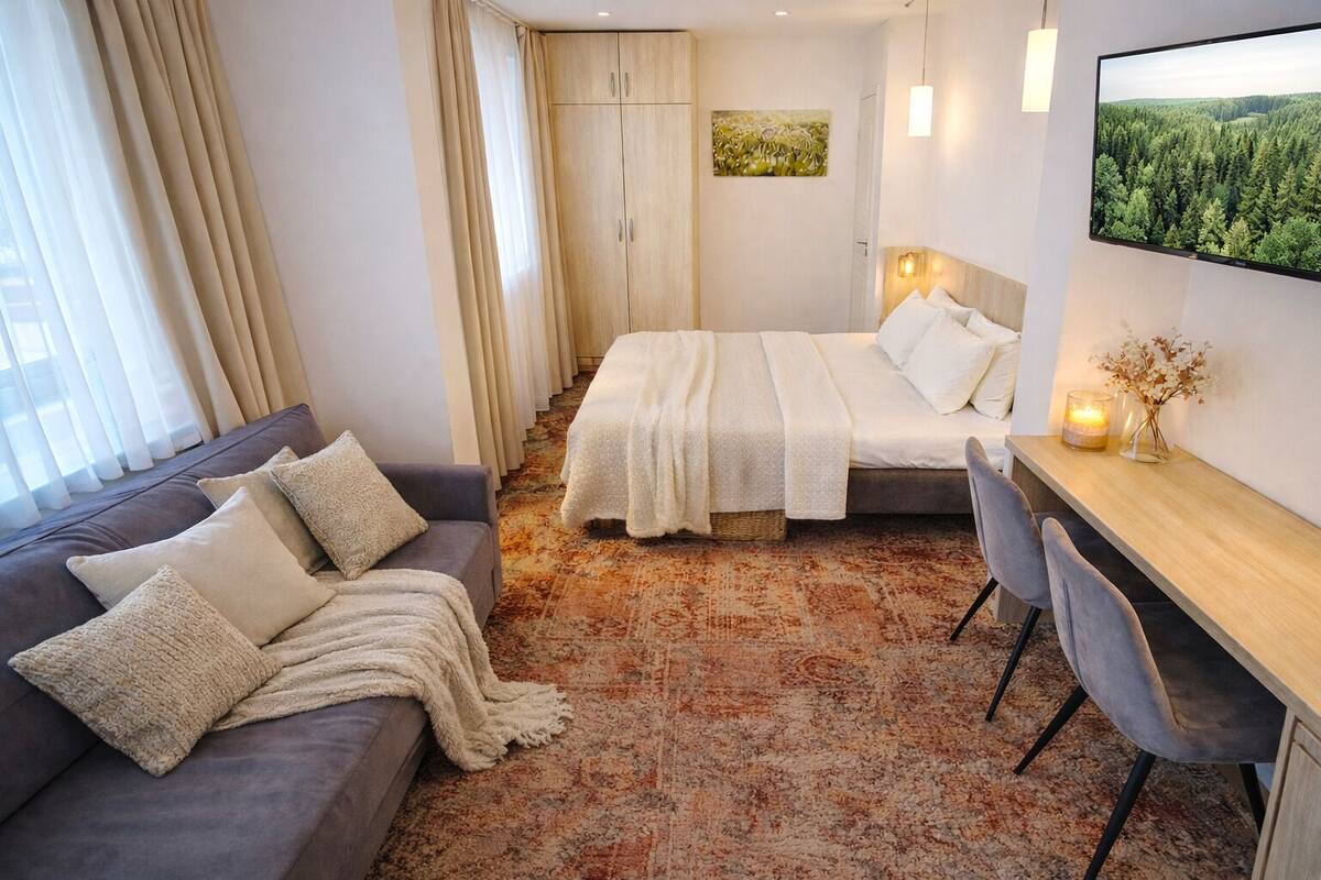 Una habitación de hotel con cama, sofá, escritorio y un ventanal con cortinas.