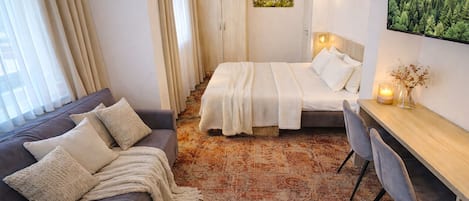 Una habitación de hotel con cama, sofá, escritorio y un ventanal con cortinas.