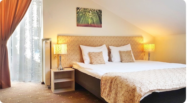 Une chambre d’hôtel avec un lit, deux lampes de chevet, une tête de lit ornée d’un motif, une petite table de chevet et une fenêtre avec des rideaux.