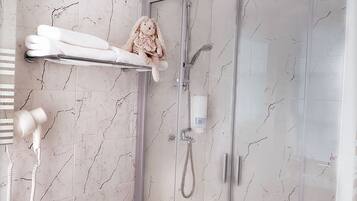 Une salle de bain avec un sol en marbre, une cabine de douche en verre, un porte-serviettes orné d’un jouet en peluche et une douchette à main.
