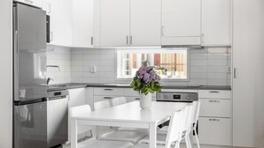 Une cuisine moderne avec des meubles blancs, un réfrigérateur en acier inoxydable, une table à manger avec des chaises blanches et un vase rempli de fleurs posé sur la table.