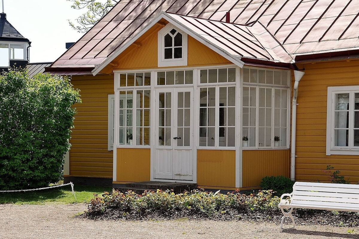 Ein gelbes Gebäude mit einer weißen Veranda und einer weißen Bank.