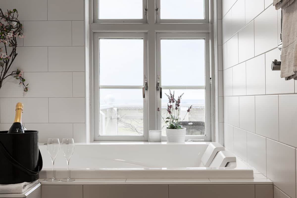 Ein Badezimmer mit großem Fenster, einer Badewanne, einer Champagnerflasche und zwei Gläsern.