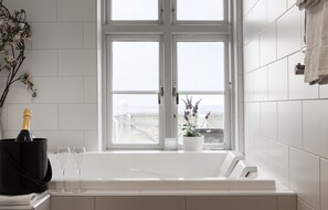 A bathroom with a large window, a bathtub, a bottle of champagne, and two glasses.
