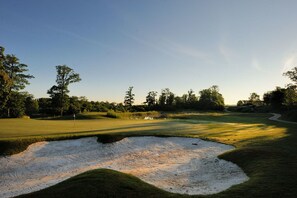 Campo de golf con búnkeres de arena, árboles y cielo despejado.