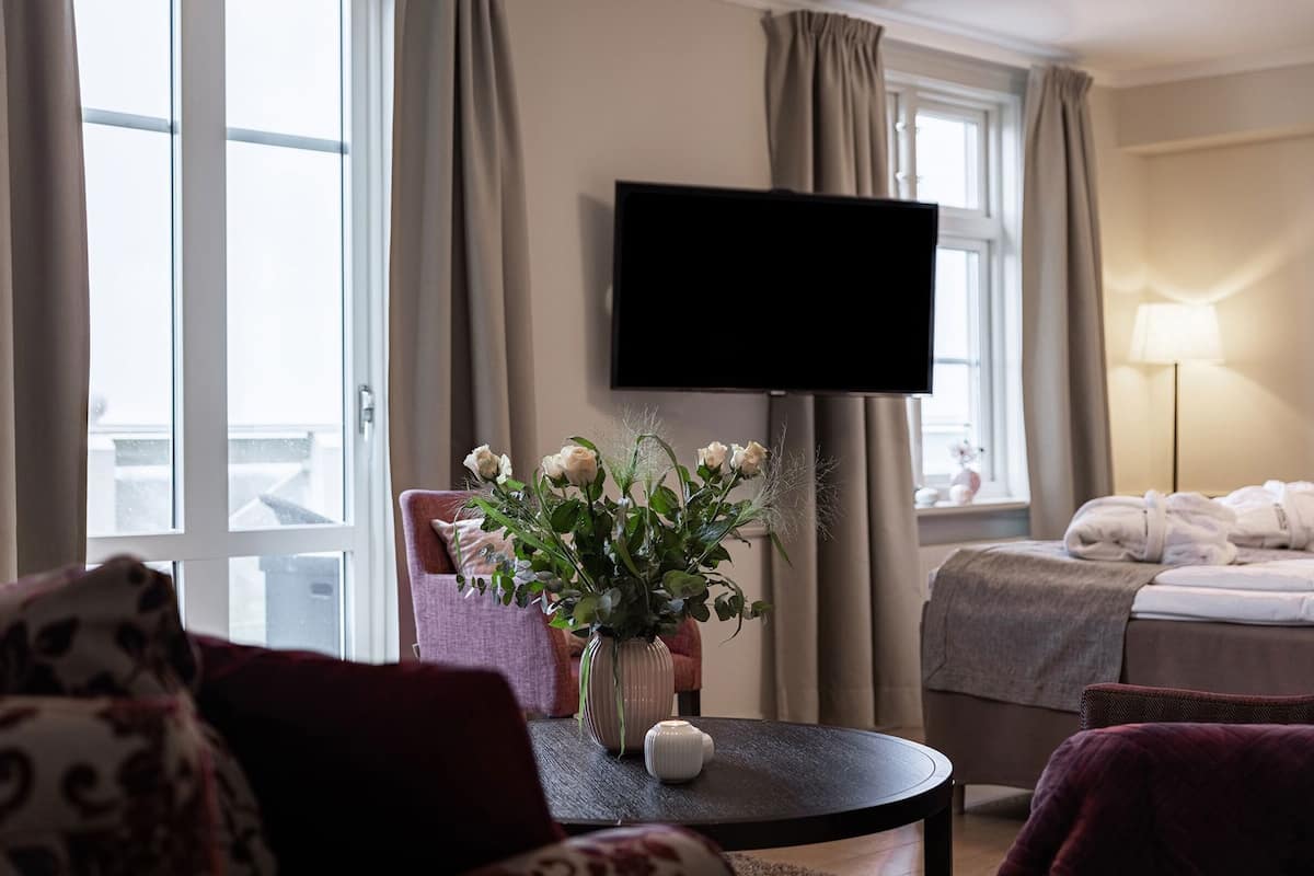 Ein Hotelzimmer mit einem Bett, einem Fernseher, einer Vase mit Blumen und einem Fenster mit Vorhängen.