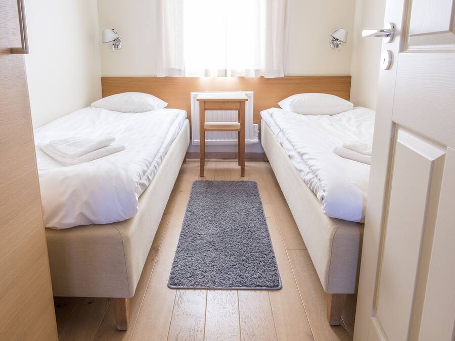 A small, clean room with two single beds, a small table, and a window with curtains.