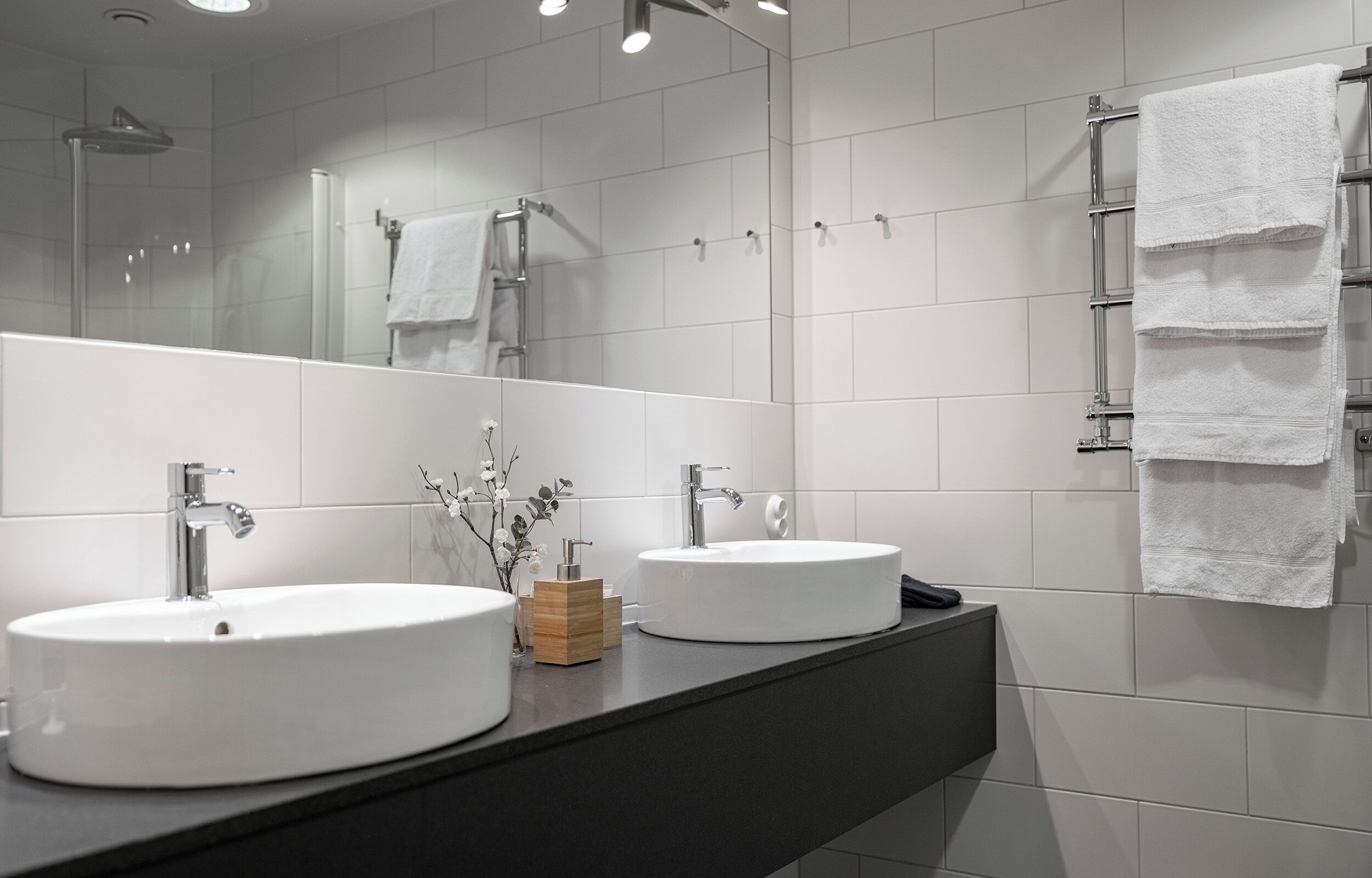 A modern bathroom with two sinks, a large mirror, and a towel rack.