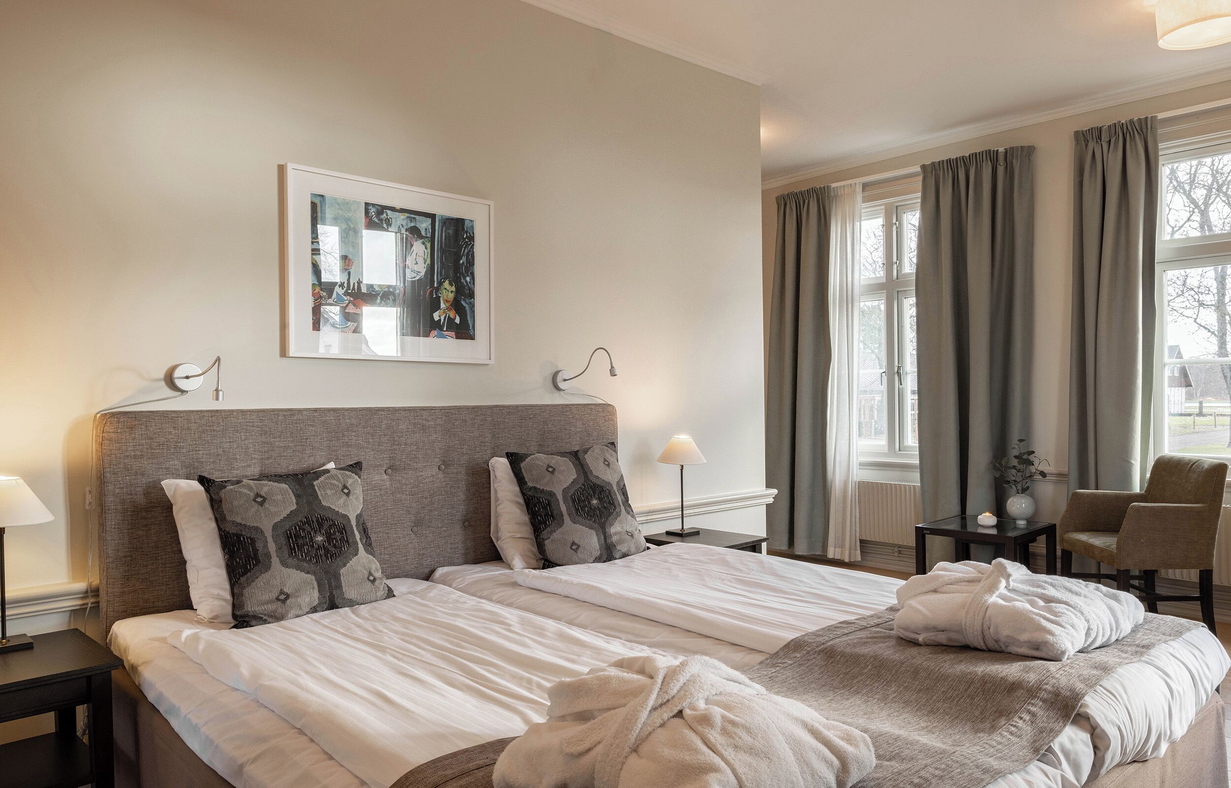 Habitación de hotel con dos camas, un cuadro en la pared, una ventana con cortinas y una silla.