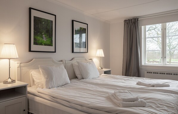 A hotel room with a large bed, two bedside tables with lamps, framed pictures on the wall, and a window with curtains.