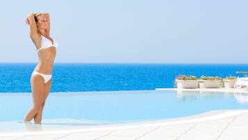 Una persona con traje de baño blanco de pie junto a una piscina con vista al océano.