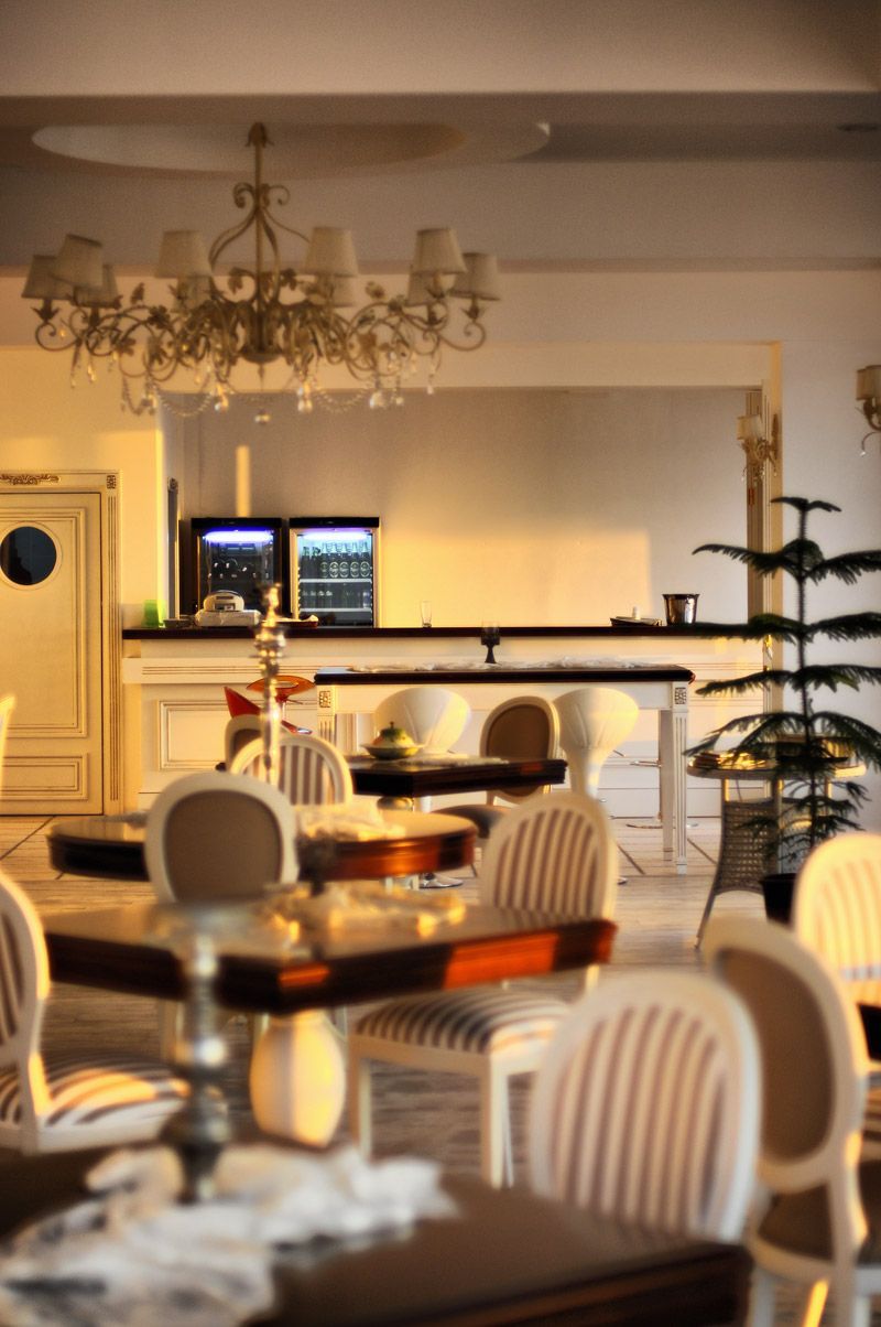 A dining area with a chandelier, white chairs, a table with a vase, and a television in the background.