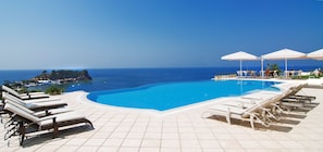 Un espace aménagé au bord de la piscine, avec des chaises longues et des parasols, offrant une vue sur une mer d’un bleu limpide et une île lointaine.