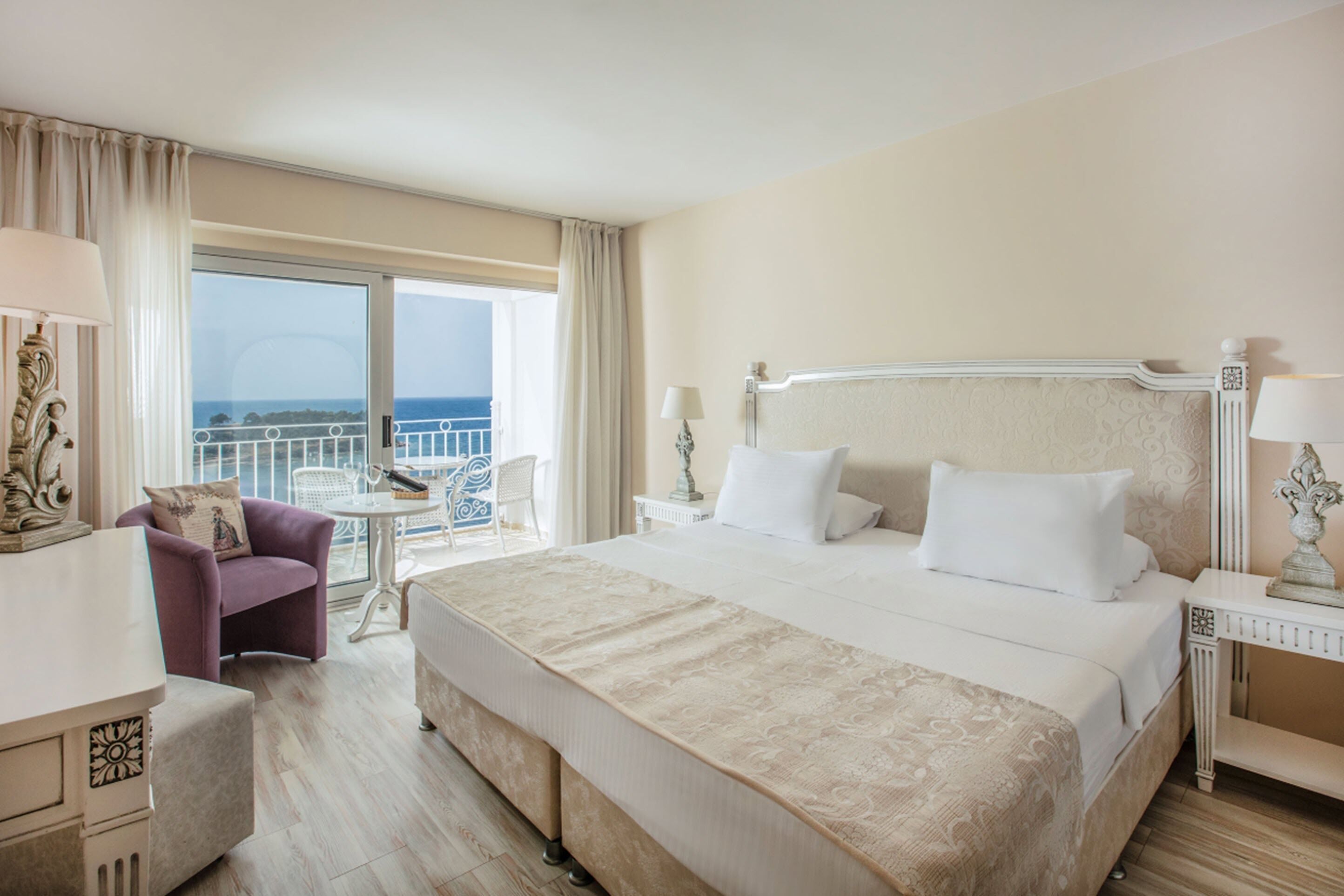 Une chambre d’hôtel avec un grand lit, une chaise, une petite table et un balcon avec vue.