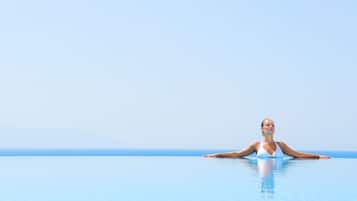 A person in a white swimsuit relaxing in a clear blue infinity pool with a view of the horizon.