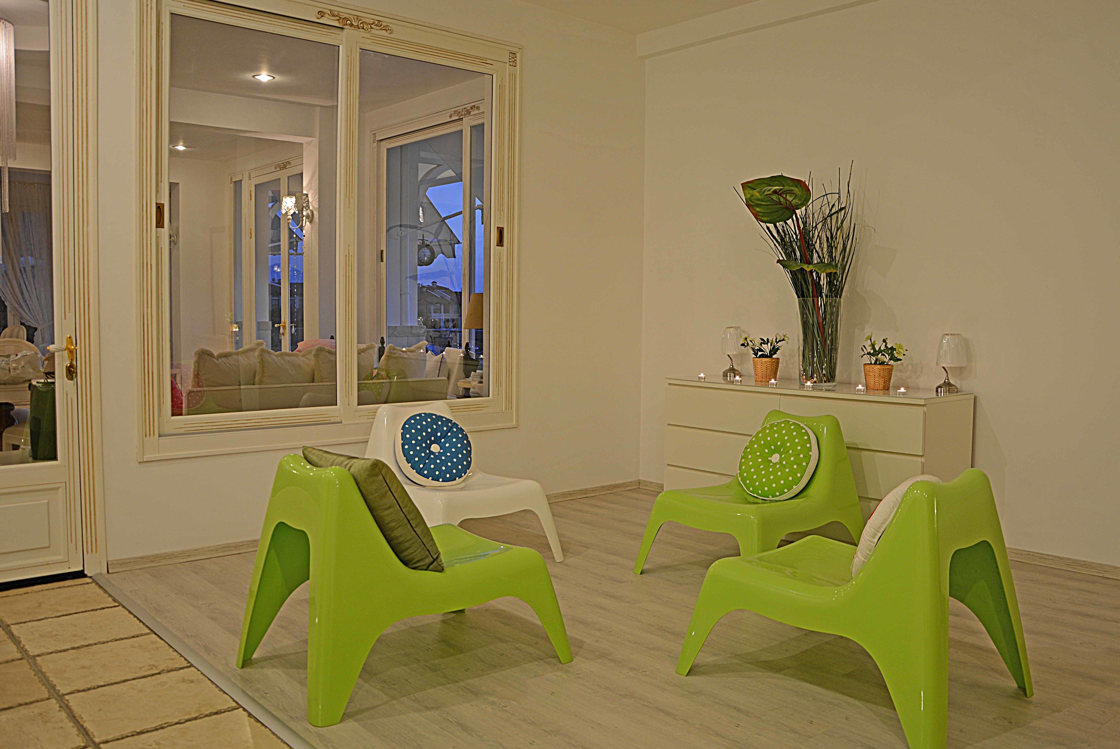 Quarto com duas cadeiras verdes, um penteado branco e uma janela grande.