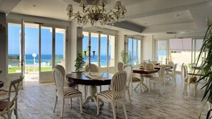 A spacious dining area with multiple tables and chairs, large windows offering a view of the sea, and a chandelier. - LaVista Boutique Hotel & Spa - Boutique Class (Kusadasi)