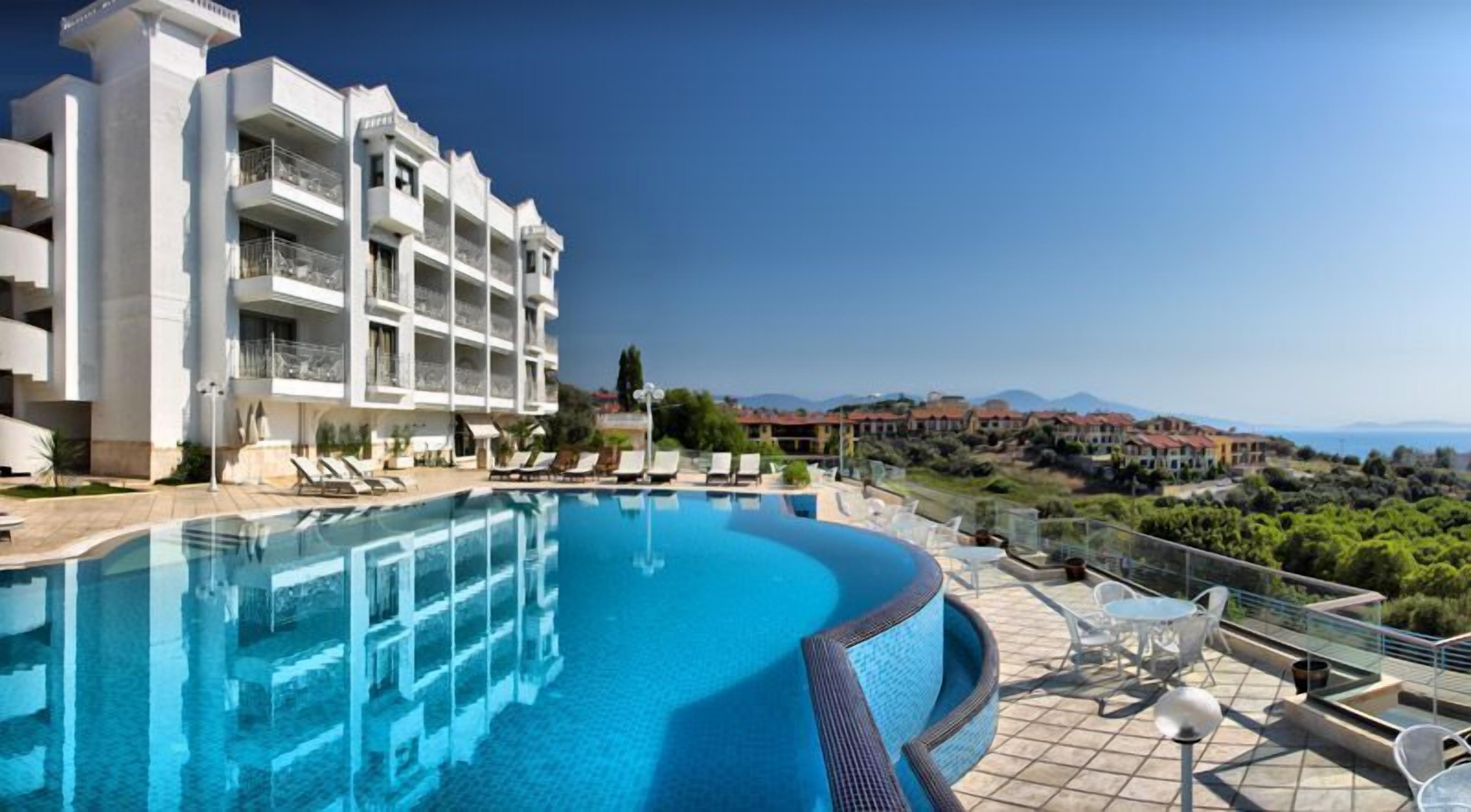 A hotel with a swimming pool, outdoor seating, and a view of the surrounding landscape.