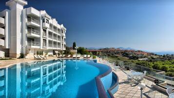 A hotel with a swimming pool, outdoor seating, and a view of the surrounding landscape.