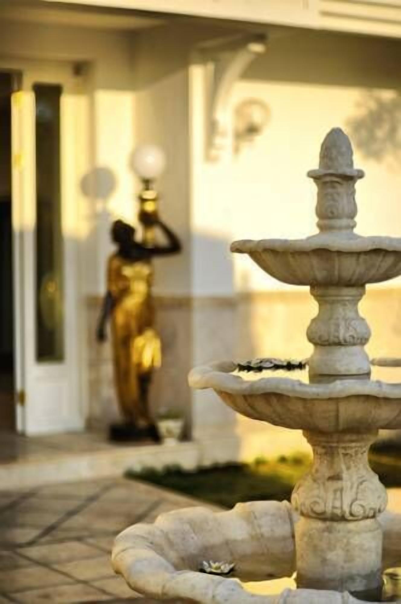 A stone fountain in a courtyard with a statue in the background.