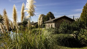 A stone house with a rustic roof, surrounded by lush greenery and tall pampas grass.