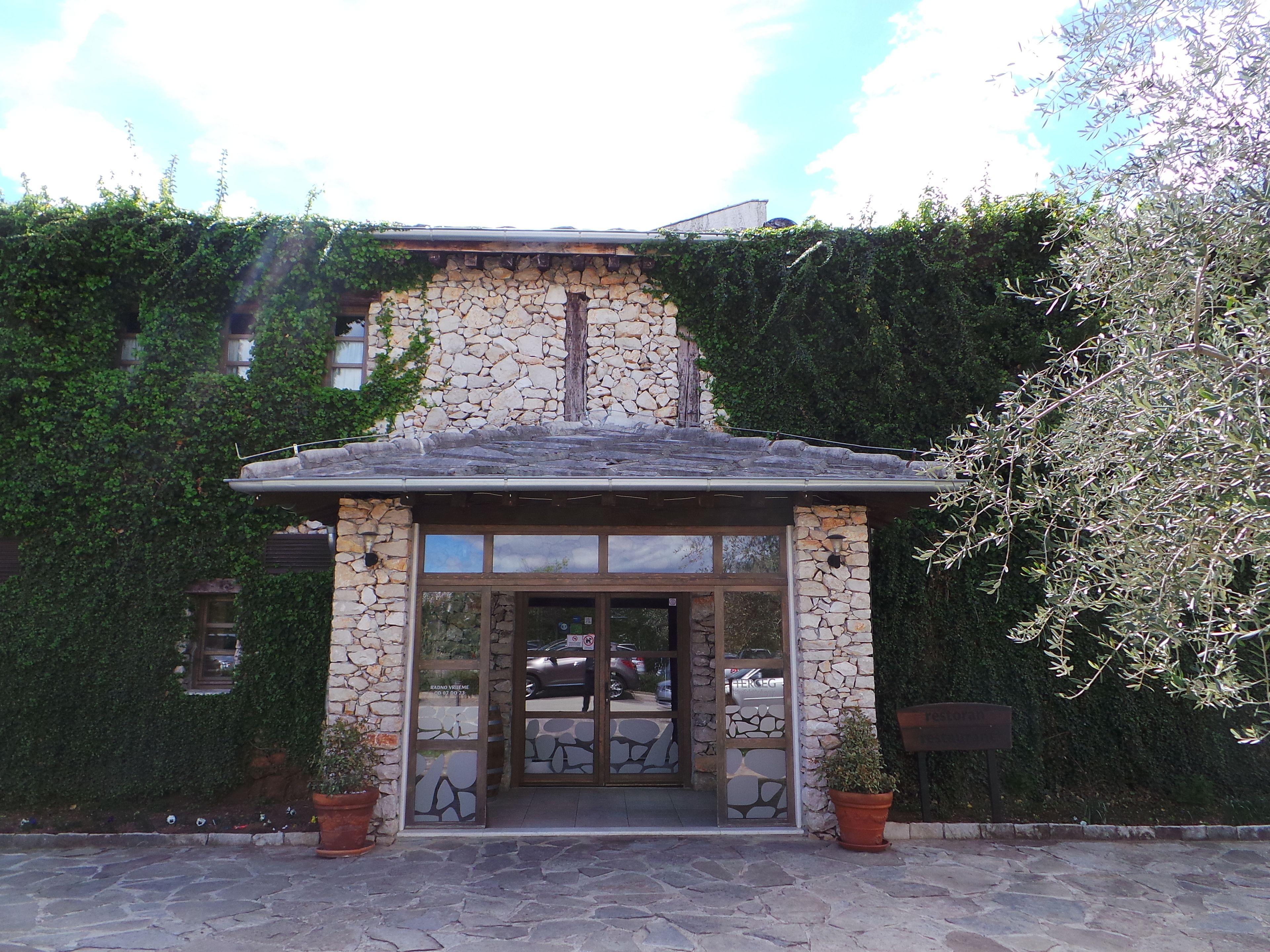 A stone building with a tiled roof, large glass doors, and potted plants at the entrance.