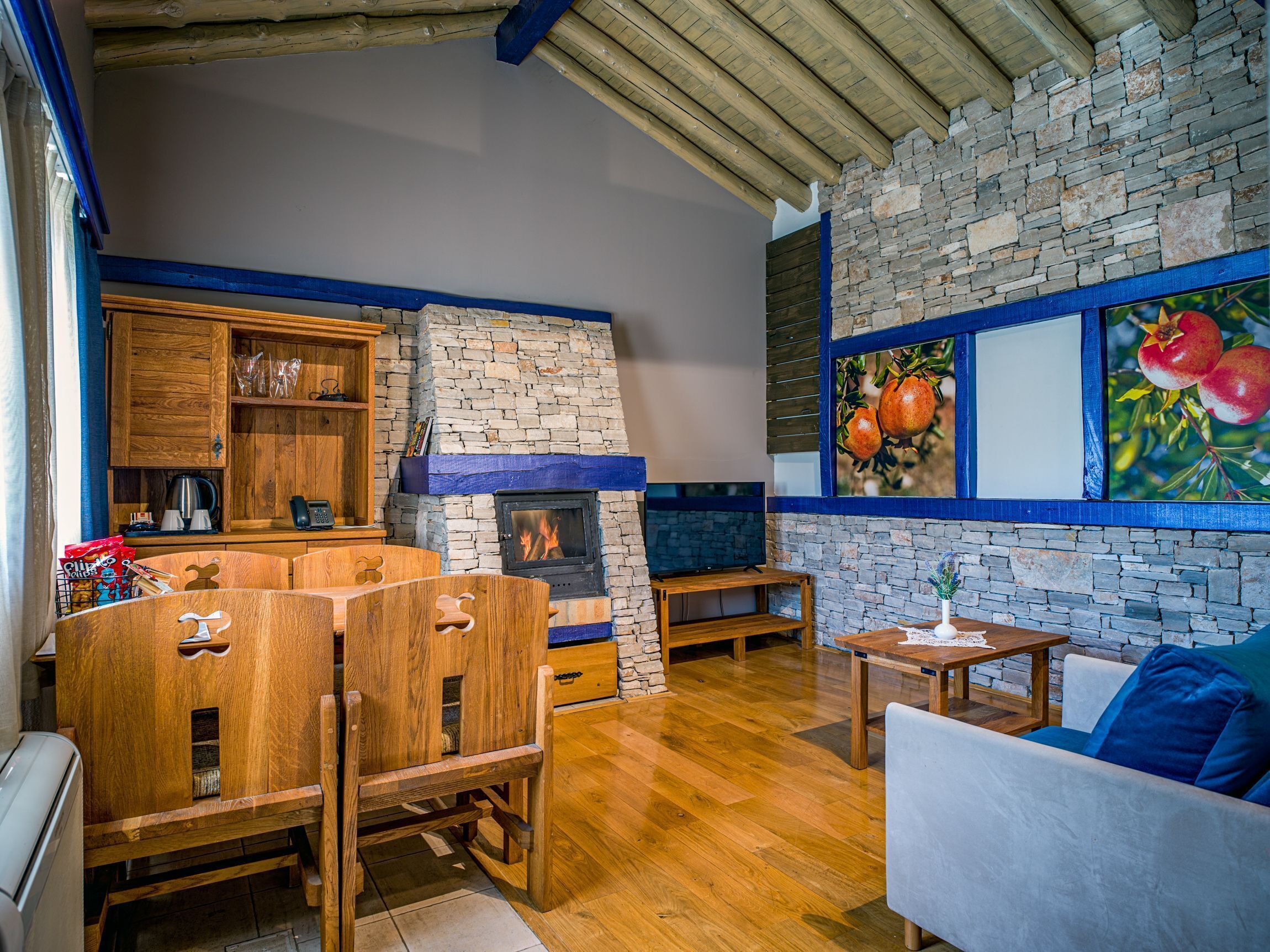 Um interior rústico com lareira de pedra, móveis de madeira e uma parede de pedra adornada com uma pintura de frutas.