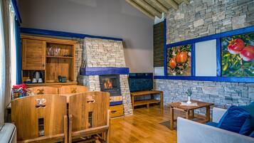 Um interior rústico com lareira de pedra, móveis de madeira e uma parede de pedra adornada com uma pintura de frutas.