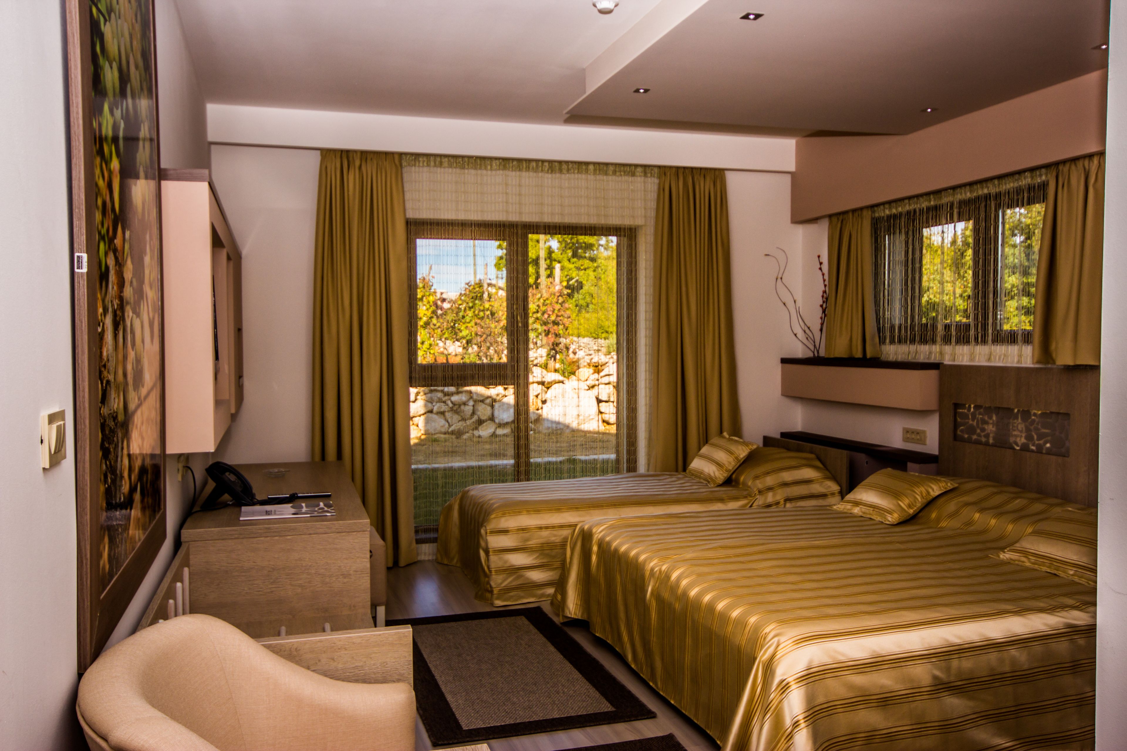 A hotel room with two beds, a desk, a chair, and a large window with curtains.